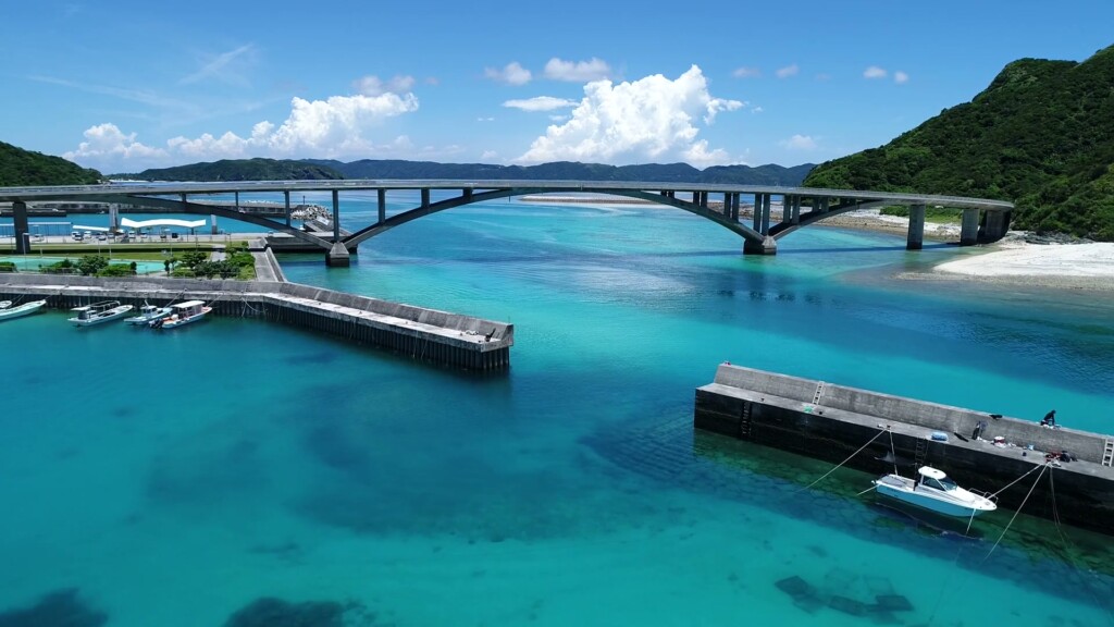 阿嘉島と慶留間島をつなぐ橋と、阿嘉の港。まわりを浅いリーフが取り囲む（ドローンによる空撮）