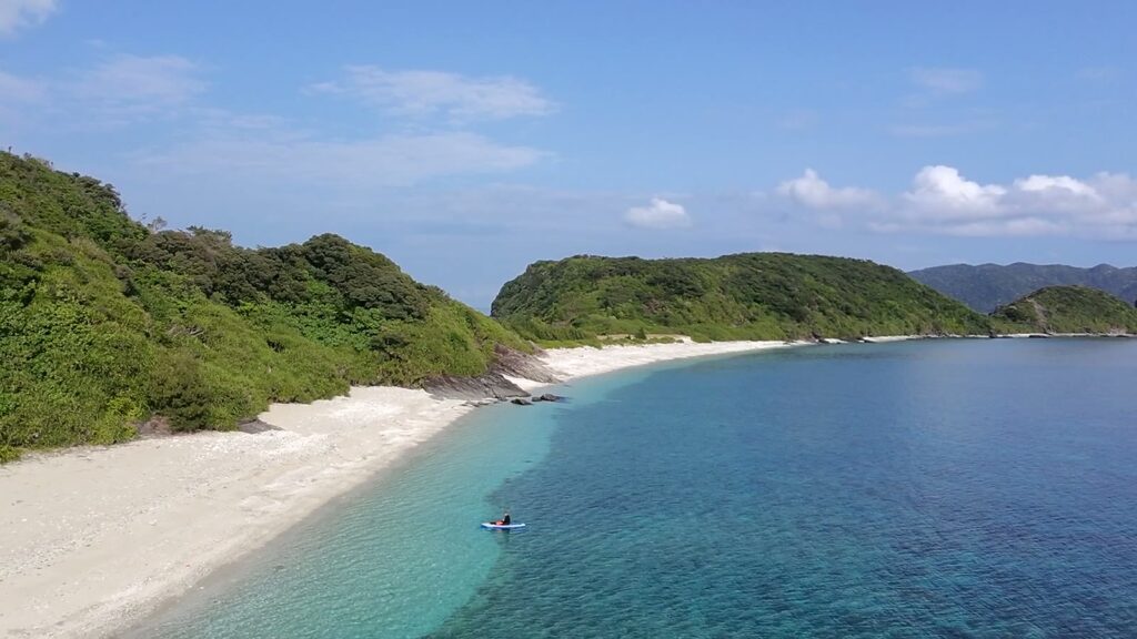 白い浜と島、沖に小さく写るSUPの人影