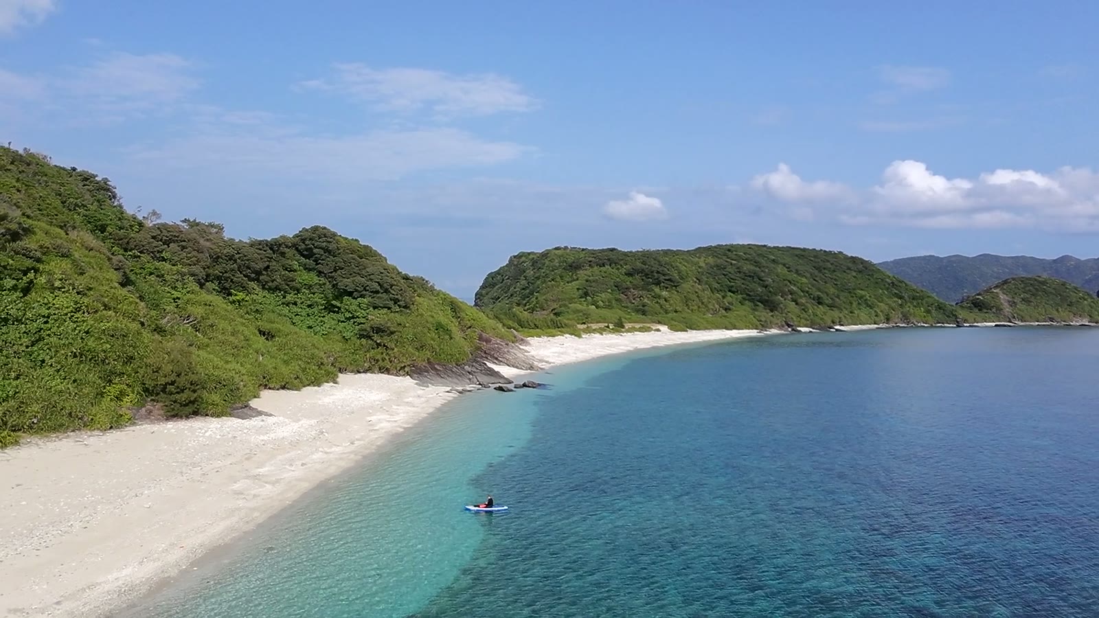 白い浜と島、沖に小さく写るSUPの人影